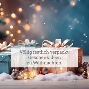 Eine festliche Szene mit drei Geschenken, die in beigem und blauem Papier mit weißem Band verpackt sind. Das Geschenk ist von silbernen und goldenen Weihnachtskugeln umgeben, die auf Schnee liegen. Im Hintergrund sind verschwommene Lichter zu sehen, die eine warme, leuchtende Atmosphäre erzeugen, wahrscheinlich von einem Weihnachtsbaum oder anderen Feiertagsdekorationen. Der Text im Bild lautet: ‘Völlig festlich verpackt! Geschenkideen zu Weihnachten.’